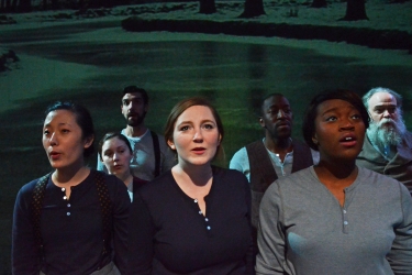 Actors singing in spotlight in front of a green and black background.